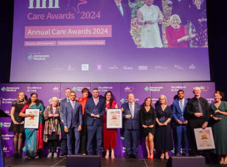 NHI Care Award Winners for 2024, standing on stage with MC Mary Kennedy