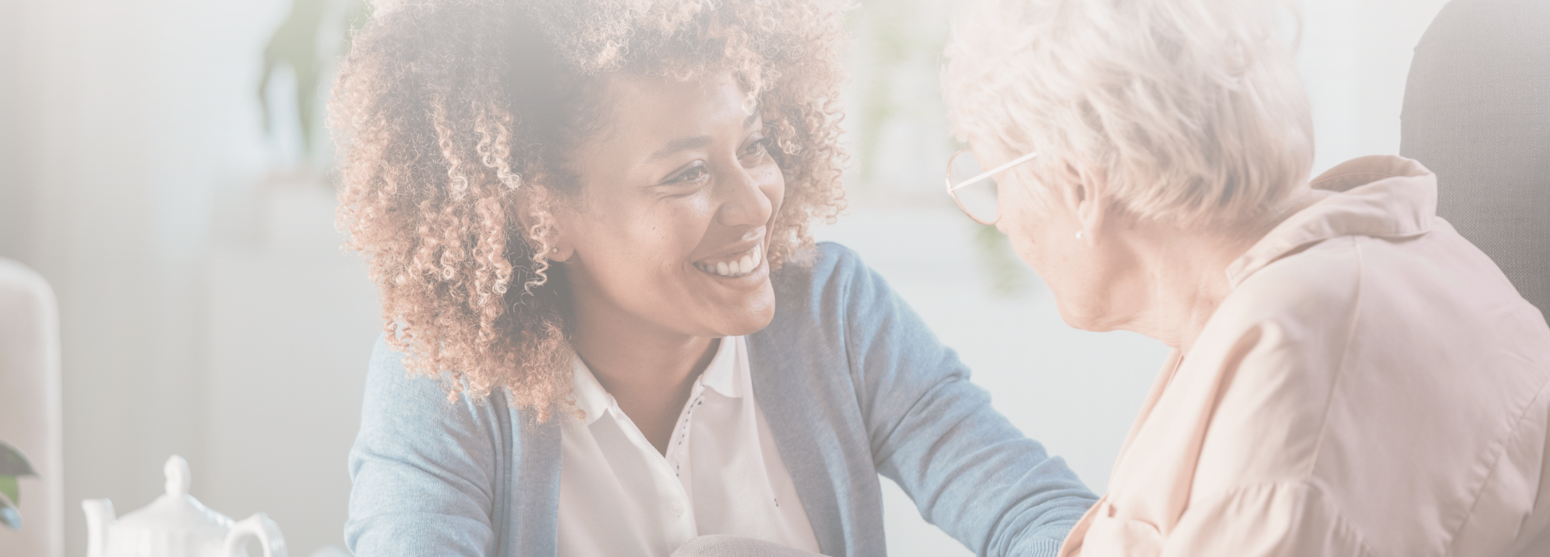 Image of a smiling caregiver engaging warmly with an elderly woman in a bright and welcoming setting, symbolizing compassion, care, and connection in healthcare and nursing home environments.