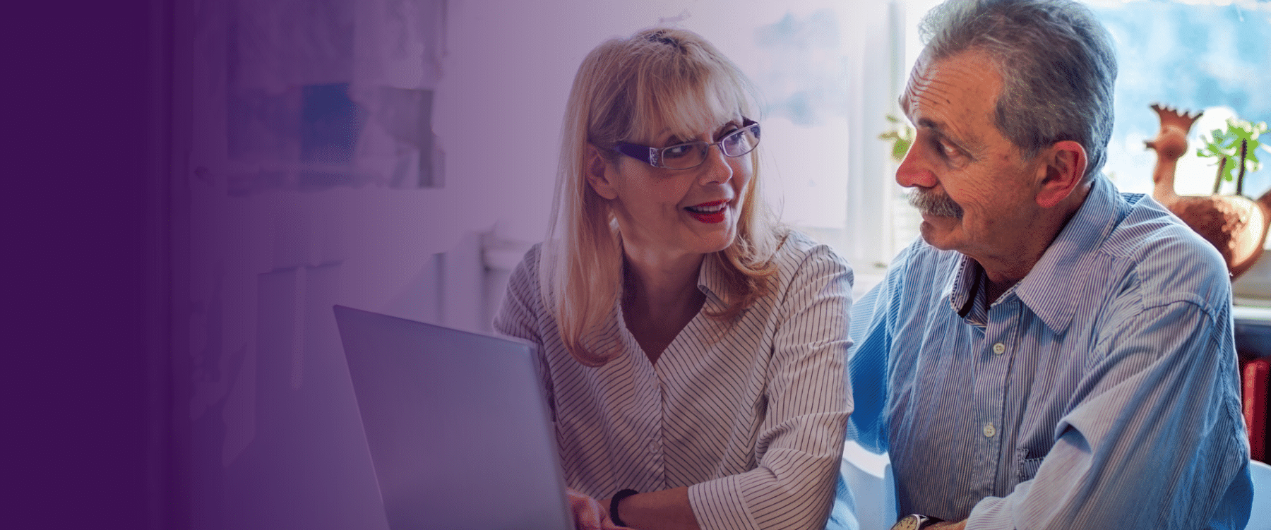 Smiling older couple using a laptop together in a well-lit home setting, with a purple gradient overlay on the left side of the image.