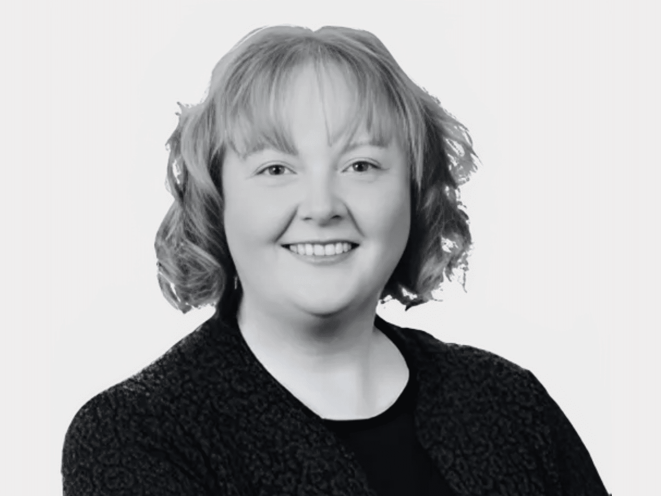 Black and white headshot of Deirdre Shanagher, Strategic Clinical Nurse Expert with Regulatory Compliance, smiling and wearing a patterned blazer over a dark top.