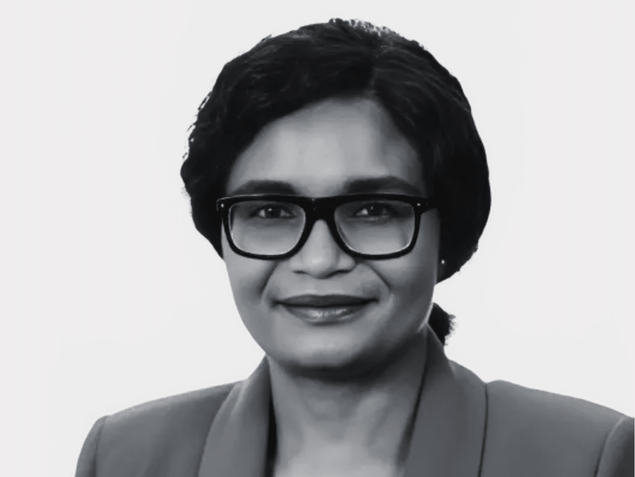 Black and white headshot of Loina Mudonhi, Accounts, wearing glasses and a blazer, with a slight smile.