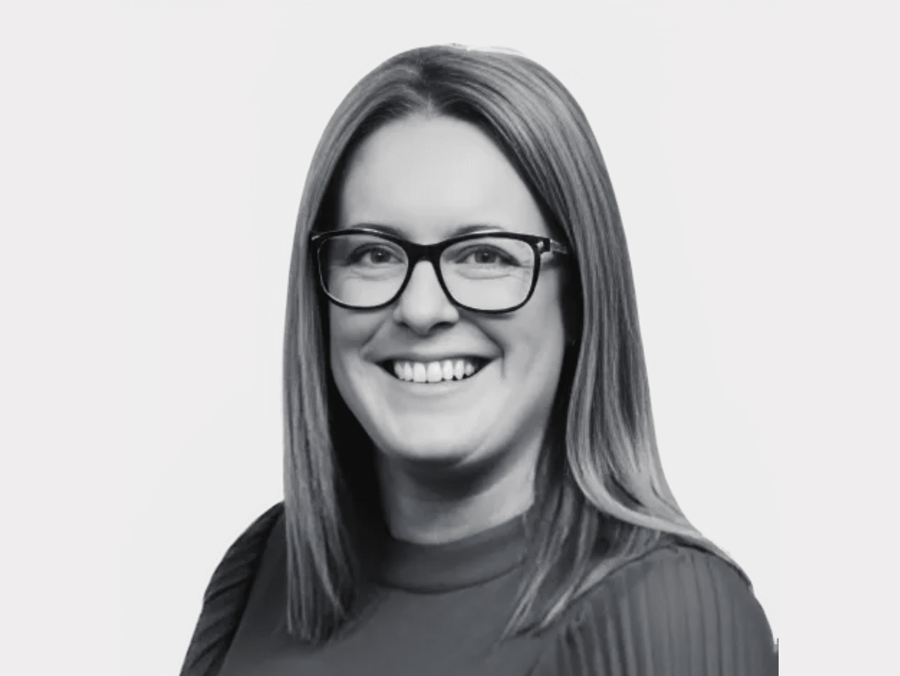 Black and white headshot of Sarah Regan, Garda Vetting Administrator, wearing glasses and a ribbed sweater, smiling.