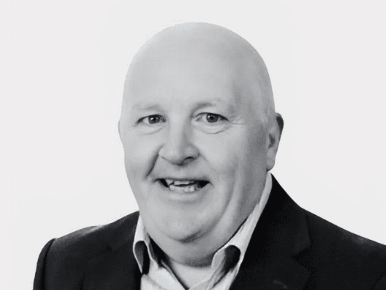 Black and white headshot of Tadhg Daly, CEO of Nursing Homes Ireland, smiling and wearing a dark suit with a white shirt.